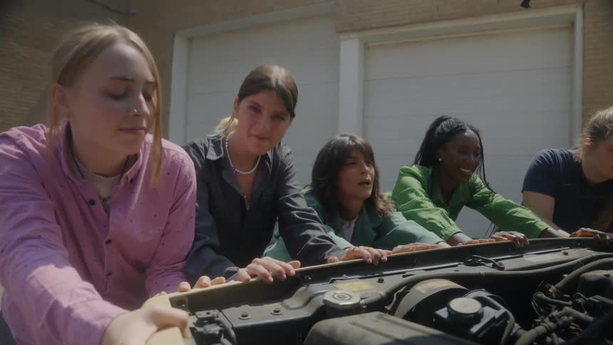 Group of 5 women pushing a broke down car