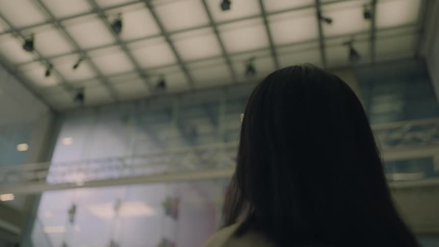 A woman wearing glasses is looking around the ceiling of a terminal building with lights just coming on