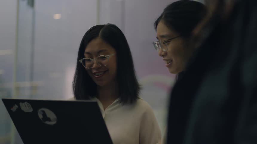 Two young woman hold a laptop while explaining