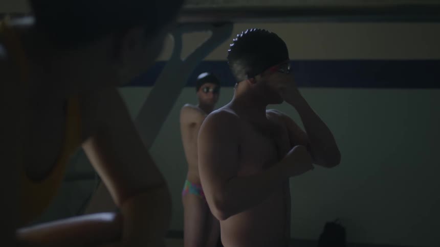 Three man standing next to a pool preparing to swim and then one of them jumps on the pool