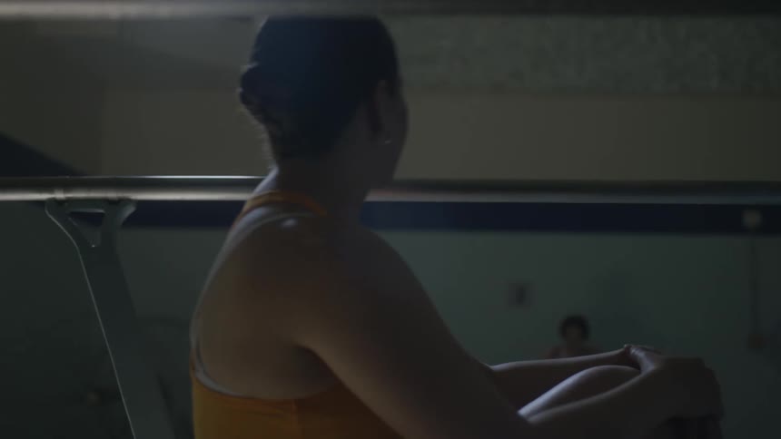 A woman sits on a diving board while another one approaches the pool