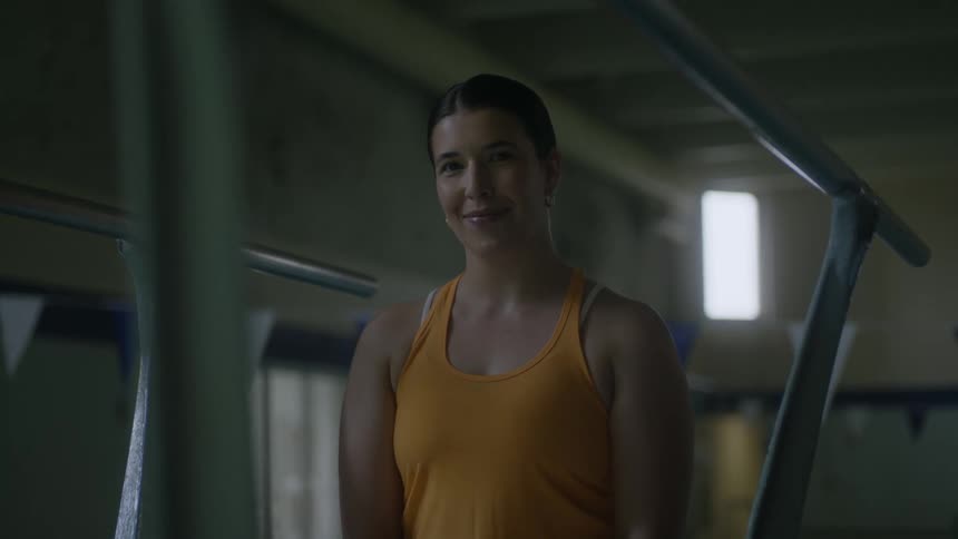 A woman wearing a yellow singlet in the gym with low light is smiling