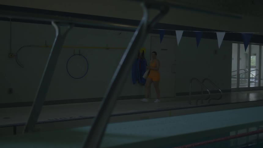 A woman walks along an inside swimming pool and joins two men who are getting ready to swim