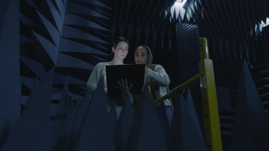 Two students read while stand on a recording studio surrounded by wedge foam
