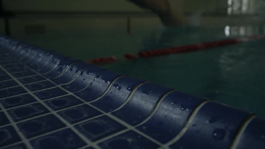 A person walks up to the edge of a swimming pool and dives in