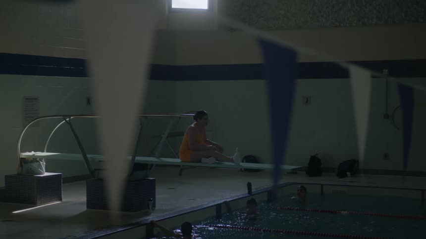 Woman sitting on a trampoline over swimmers floating on an olympic pool