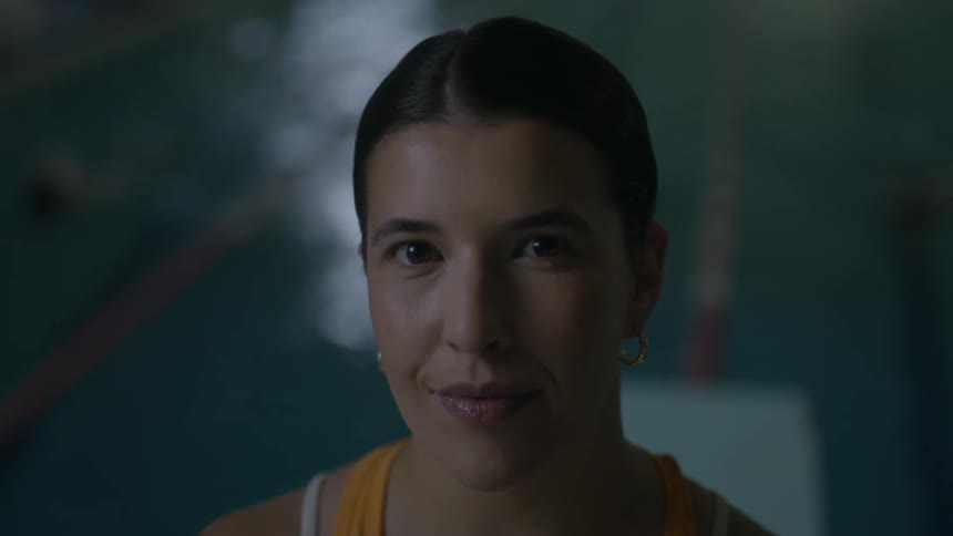 A woman subtly smiles as the water ripples in the swimming pool behind her