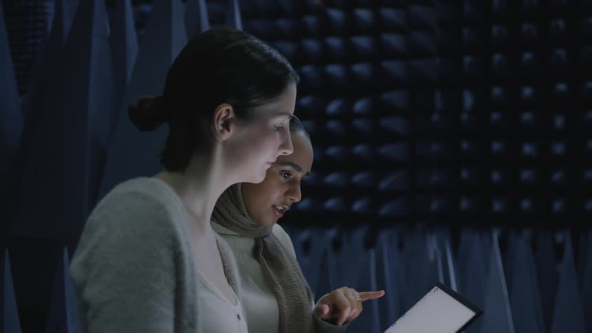 Two women stand together while one holds a laptop in her hands