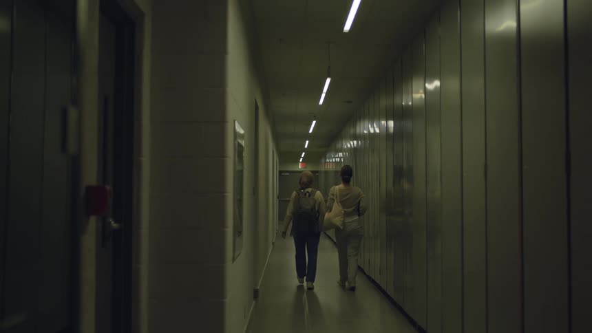 Two women walking down a lit hallway both carrying bags on their shoulder