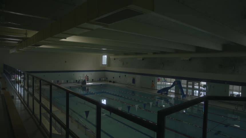 An indoor swimming pool in a large building as people walk along the edge of the pool