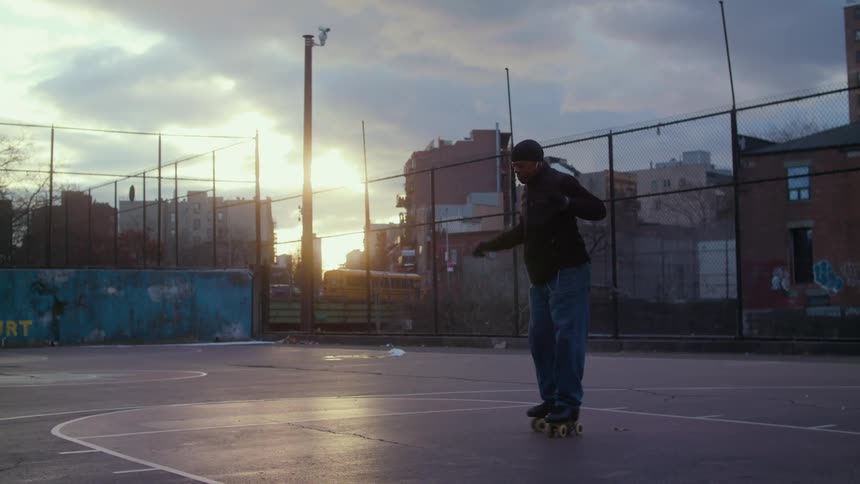 Man wearing roller skates dances on a basketball court in town at evening