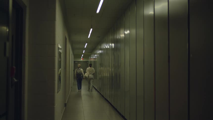 Coworkers walk down long corridor lit by fluorescent lighting
