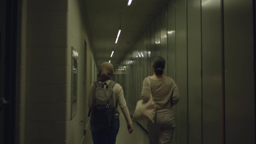 Two women walk together through a long narrow hallway