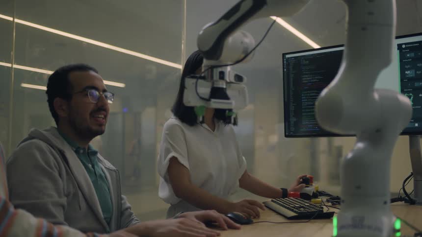 Two asian women and a men testing a robotic arm over a table