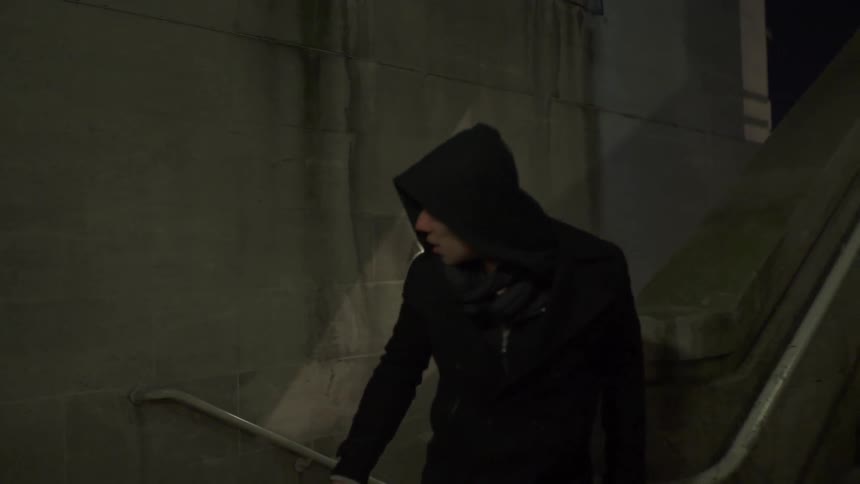 A man in a hooded coat looks behind him as he runs up stairs