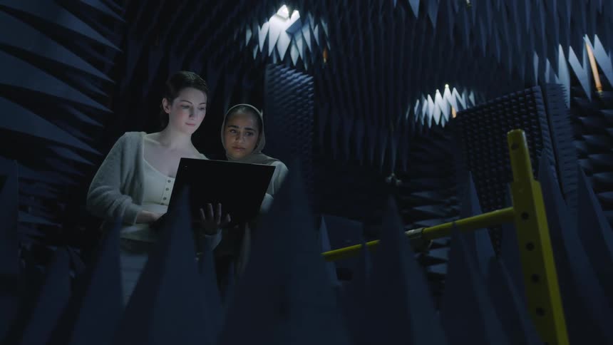Two women consult over laptop in industrial lab lined with spiked foam