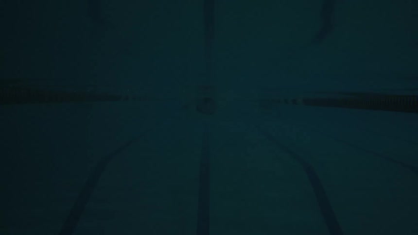 A male swimmer in a pool swims quickly from one side to the other