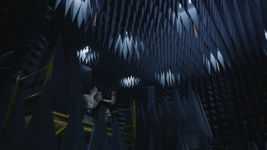Two people working behind a stage on a platform with lots of lightening that are switched off