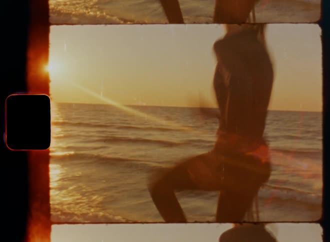 Female sportsman steps and runs in place with dynamic arm hand movement on coast under glaring sun light causing bright lens flares as waves roll onto beach on vintage 8mm film with a nostalgic vibe