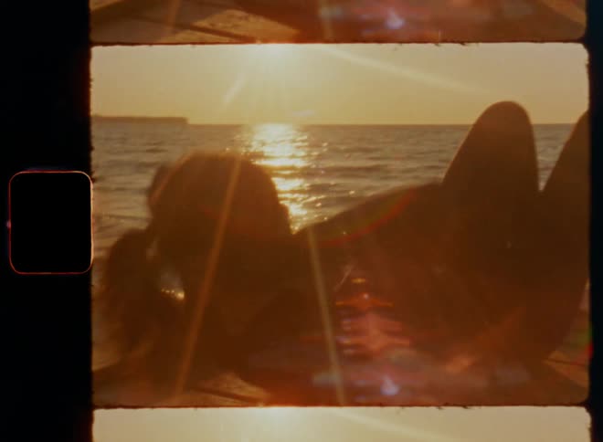 A body conscious woman doing challenging sit ups with high pulse on a boardwalk made of wood next to the ocean as the sun is setting over the wavy waterfront of the sea on Super-8 mm film