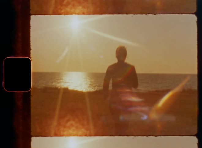 Female jogger wearing fitness sportswear runs and sprints across grass field towards the open ocean as the water of the sea reflects bright sunshine at the horizon and creates a vintage lens flare on Super-8 mm film