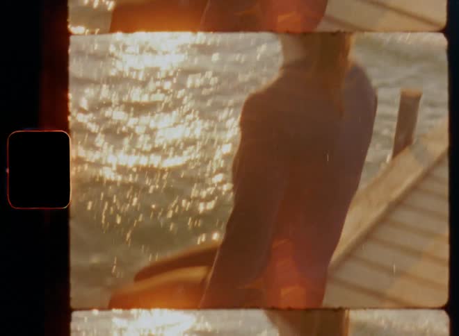 Sportswoman with brown hair in a pony tail resting at a port as the sun rises on a beautiful spring day creating shadows on the wooden deck and bright reflections on the water surface that is moving in a dynamic way due to waves caused by a mild breeze