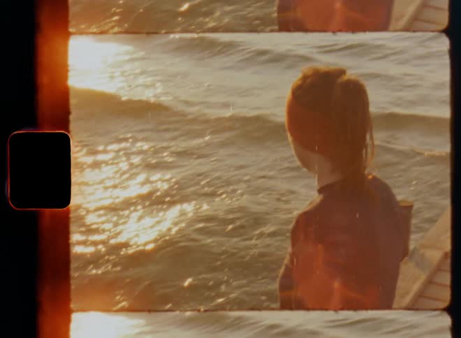 A young woman sitting on a wooden deck and taking a break with her legs and feet with running shoes or sneakers hanging over the edge and dangling over the water as she looks out into the romantic sunset by the sea enjoying inner peace