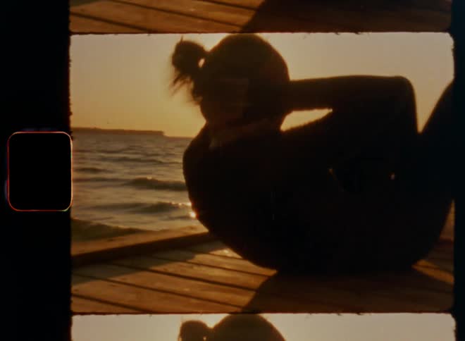 Sporty female woman athlete with ponytail doing crunches for a fitness challenge on pier is silhouetted against the scenic romantic sunset at lake or coast during golden hour enjoying joy of life vitality and good vibes during an evening workout