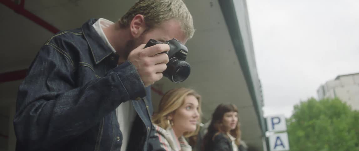 Group of people stand at a railing in a parking garage as one man takes a photo with a camera