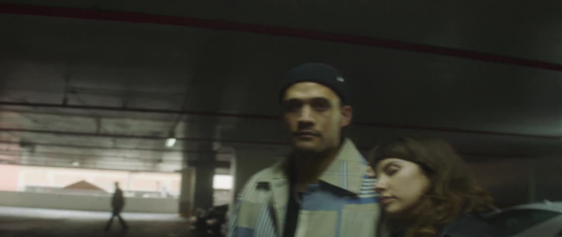 A woman leans her head against her boyfriends shoulder while standing in the parking garage