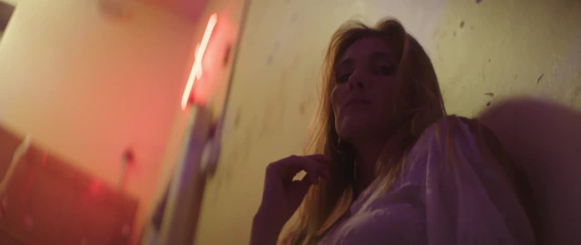 Woman wearing a nose ring and hoop earrings leans against the wall as she touches her hair with her fingers