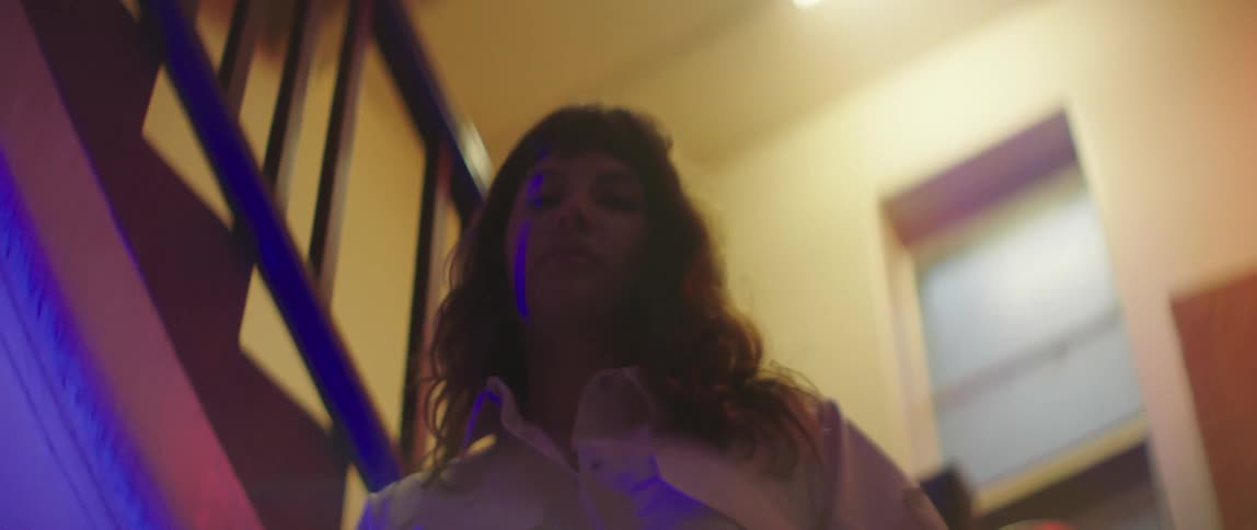 A blue light shines on a woman standing in a stairwell