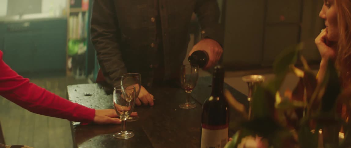 A woman pushes her wine glass closer to a man pouring from a bottle