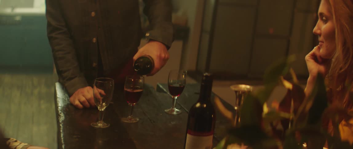 A man at home pours a glass of wine and hands it to a woman and then pours another glass