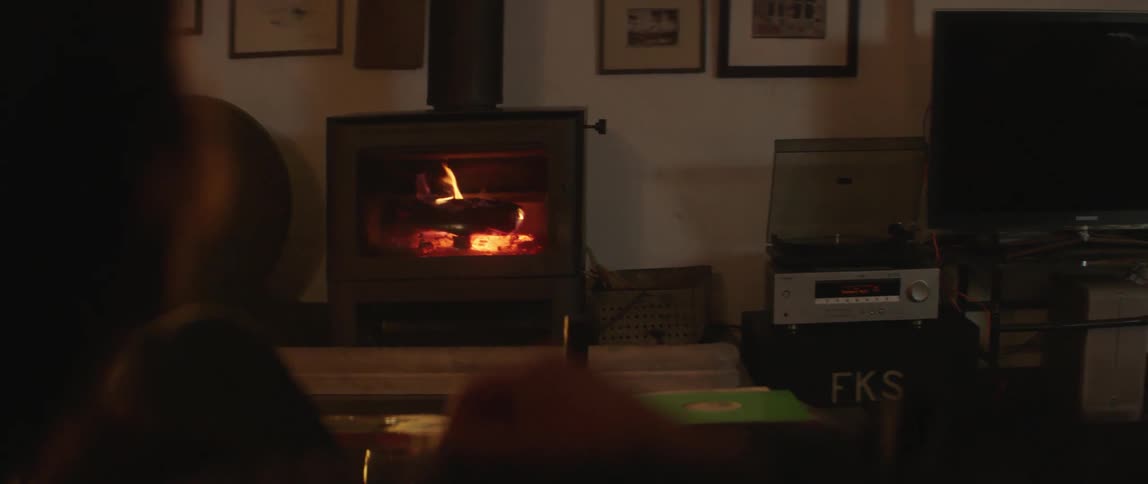 A man sits at home in front of the fireplace with a beer