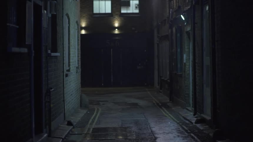A dark alley has some lights on the wall ahead