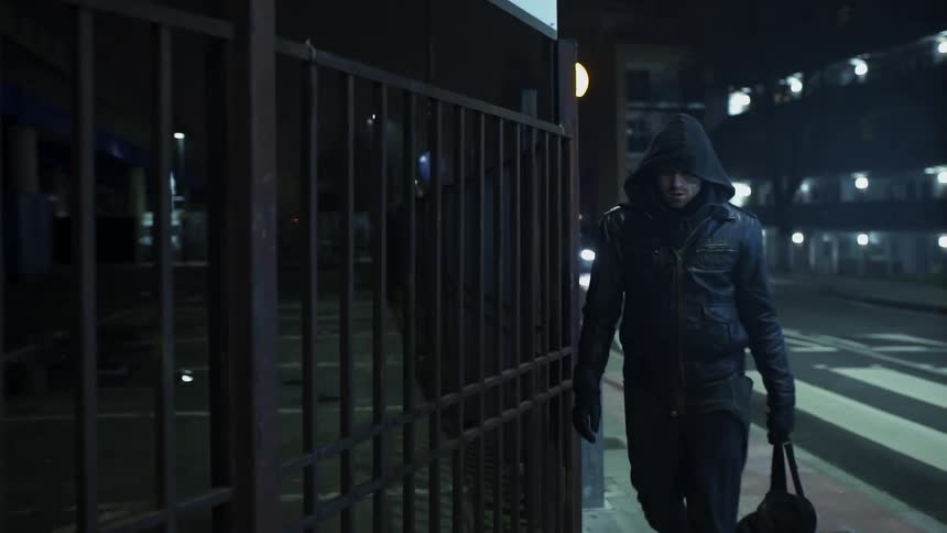 A man wearing a hoodie and carrying a bag is walking on a sidewalk
