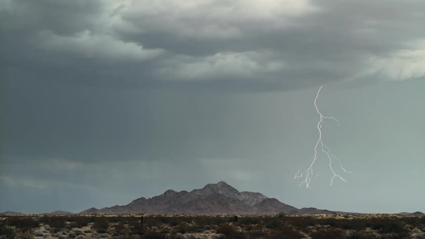 Lightning streaks through the cloudy sky above a mountain in the countryside during the day