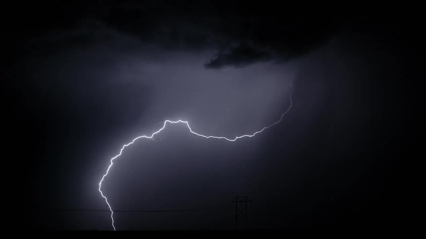 In the cold dark night a lightning strike pierces through the sky briefly illuminating an electric hightension line