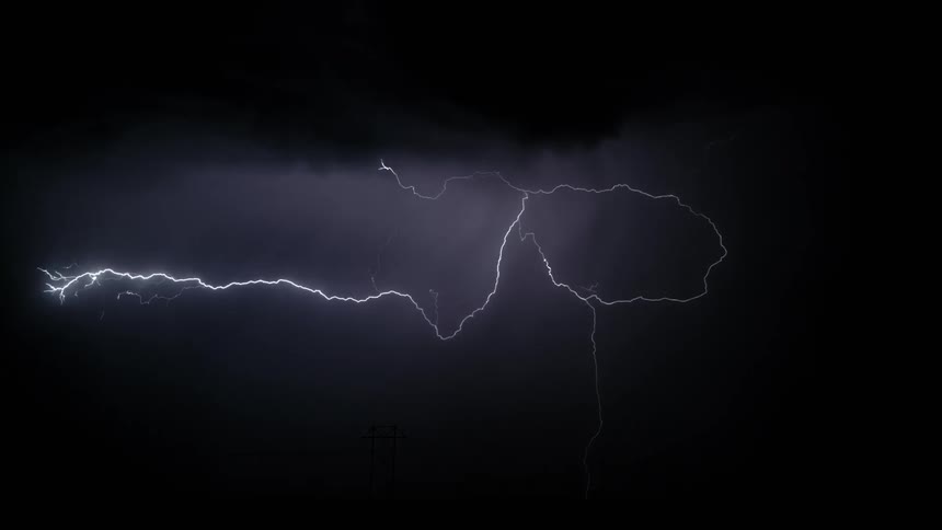 Lightning bolts winding through storm clouds and toward the ground at night cast utility poles into silhouette