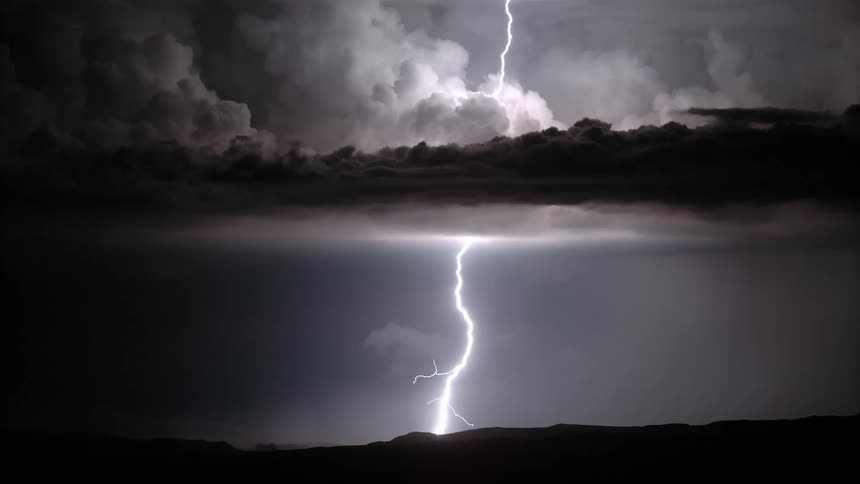 Lightning strikes mountains through clouds at night