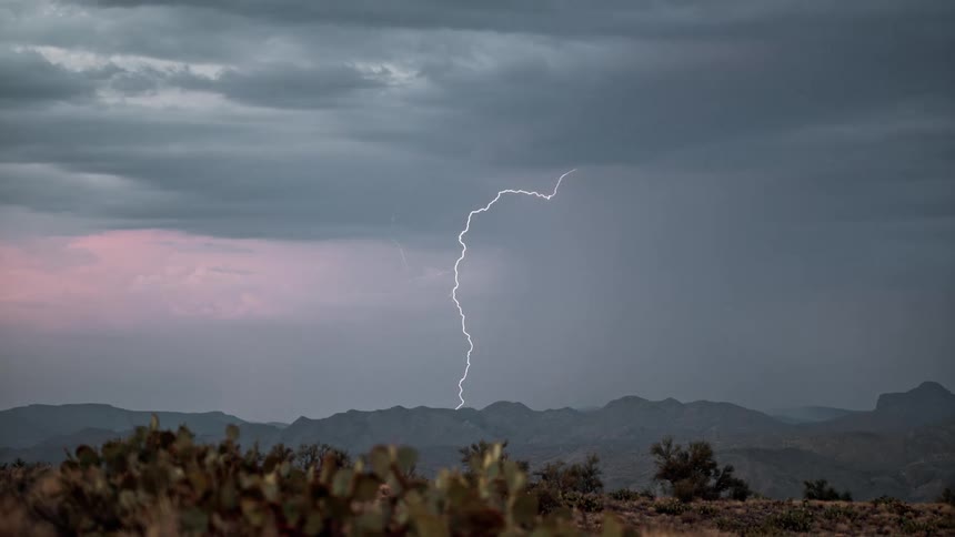 Multiple bolts of lightning descend from storm clouds above a mountain range