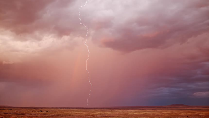 Lightning streaks through the cloudy sky above a grassland in the evening
