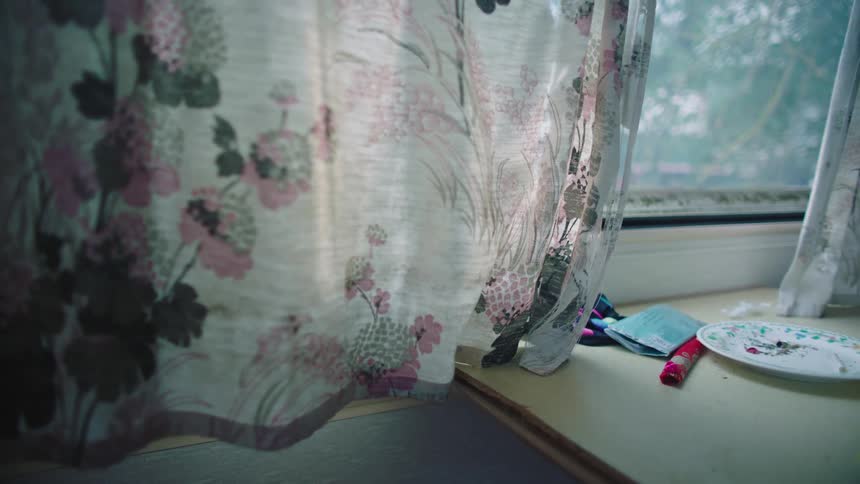 Window curtains with a flower pattern hang above a table near a window