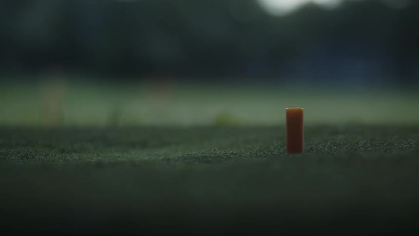 Golf club hits a yellow ball over a tee in a golf course