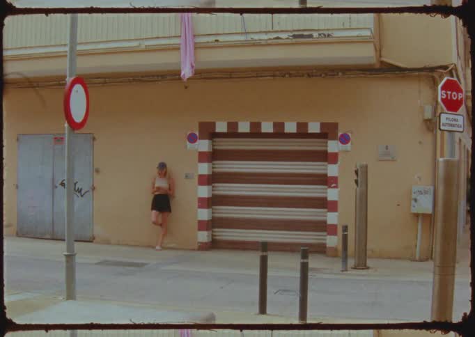 A young woman standing against a building near a loading door in the middle of the day