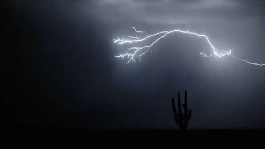 A heavy lightning storm above a desert cutting through the night sky going from cloud to cloud in slow motion