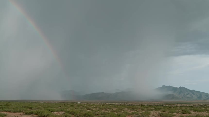 Lightning and rain fall next to a rainbow over the mountains in the plains