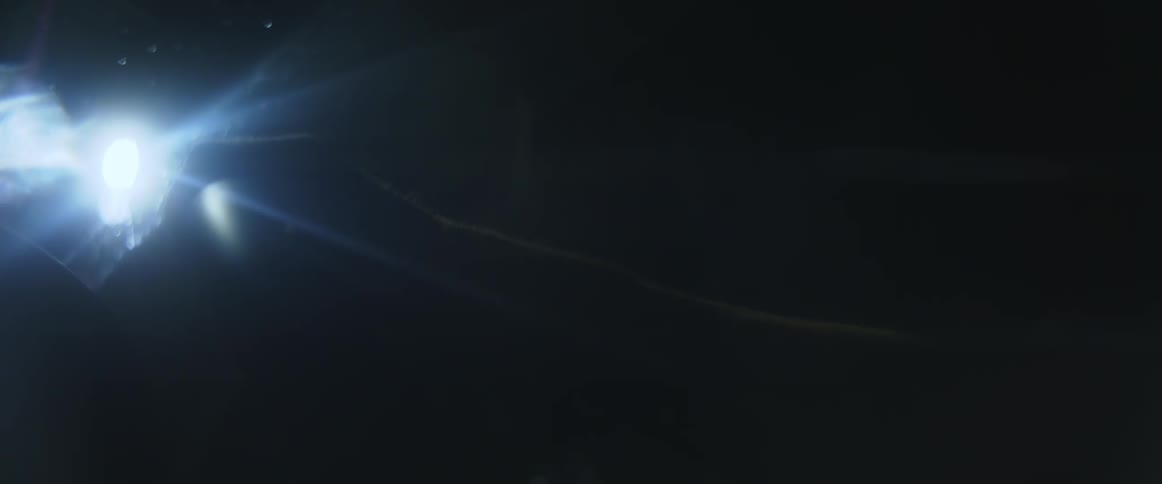 Close up of a persons hand on a steering wheel driving their car at night as street lights flare in the car
