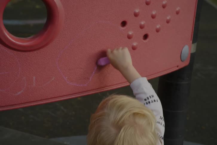 Child drawing with crayons on a red board